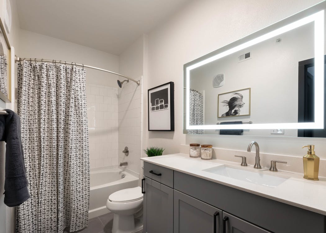 AMLI Quadrangle bathroom with grey vanity and a white countertop with a toilet and shower tub with black and white curtain