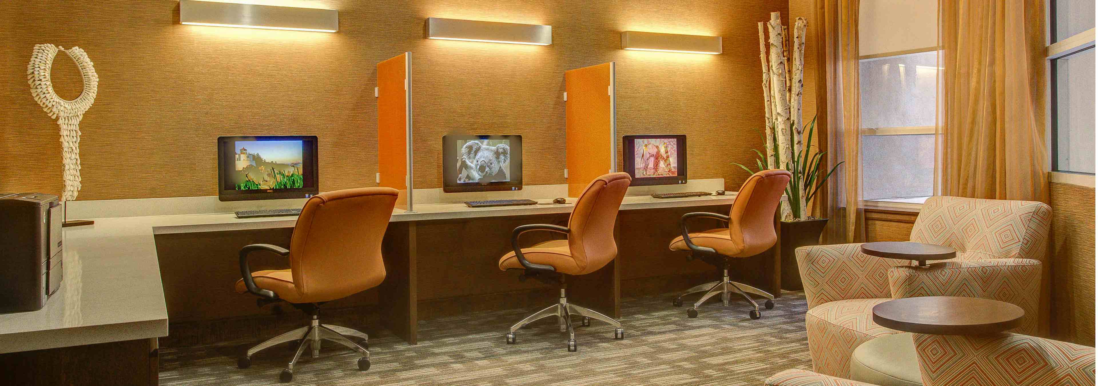 A business center at AMLI Riverfront Park apartments with several computers with rolling chairs as well as other seating area