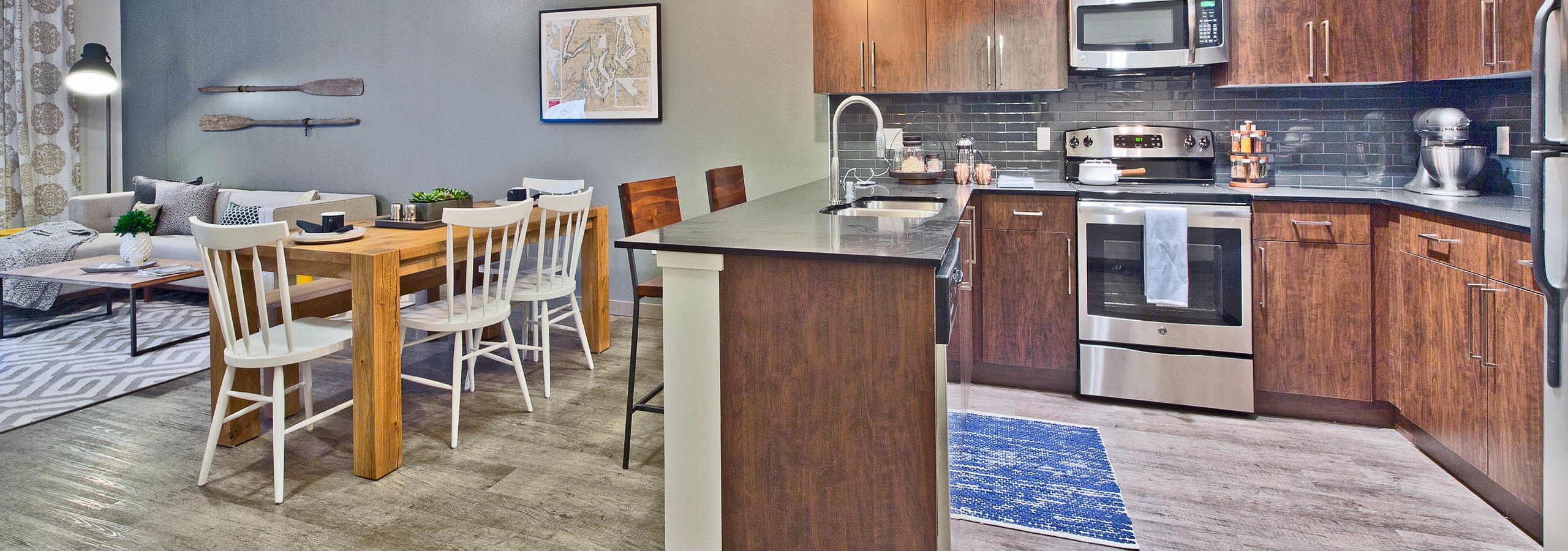 Interior view of AMLI Mark24 apartment kitchen with dark cabinets black quartz counter tops light laminate floors and view of living room