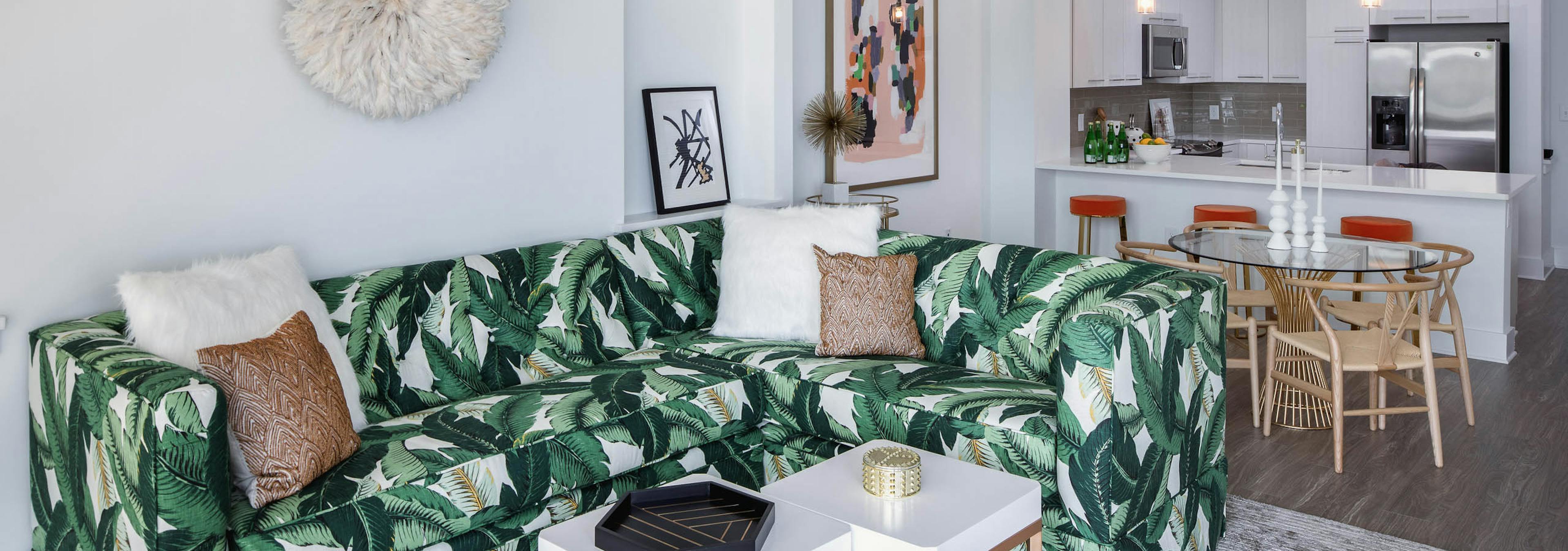 Alternate view of AMLI 3464 living room with palm branch sofa and the kitchen with a counter and barstools in the background