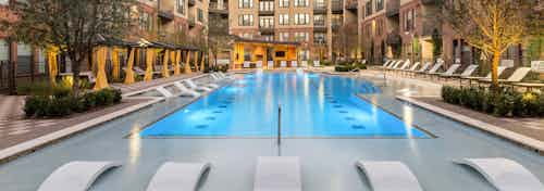 Exterior view of AMLI West Plano pool with white lounge chairs and a bright sunny view of surrounding trees and buildings