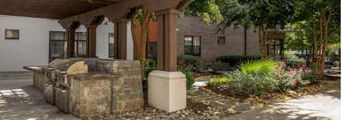 Outdoor grilling area at AMLI Old 4th Ward with stainless steel grills under a shaded trellis next to landscaped trees