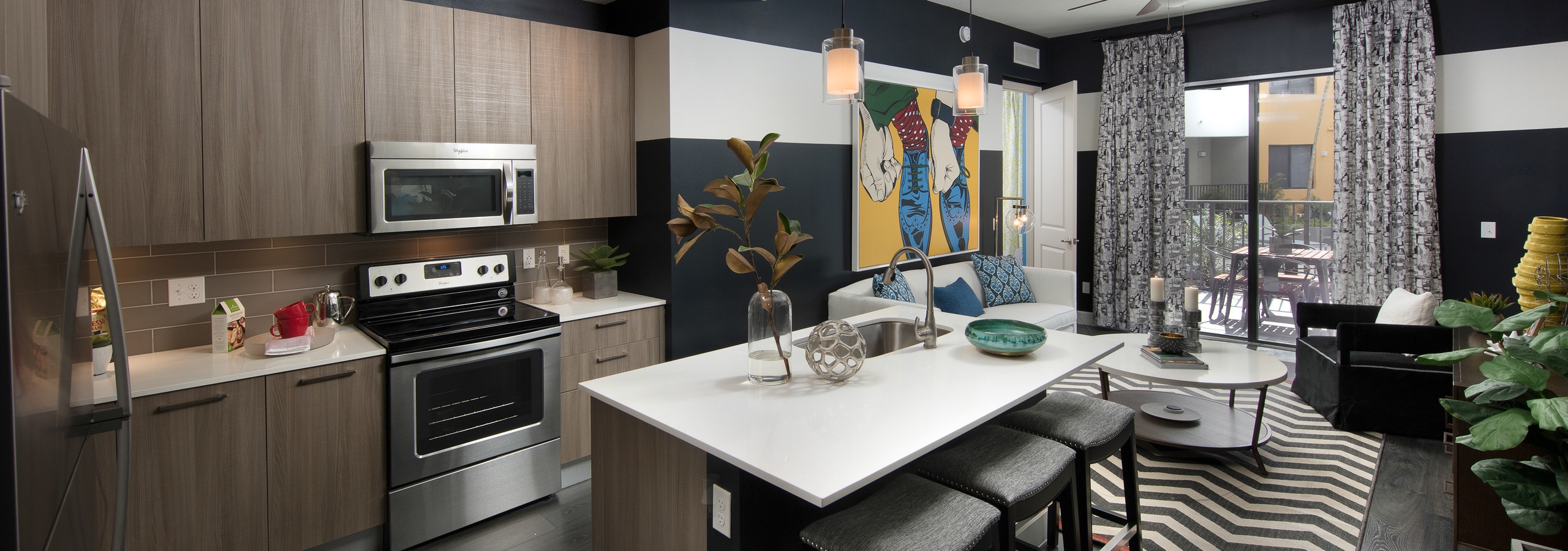 AMLI 8800 apartment with island kitchen with stools, stainless steel appliances, wood cabinetry and peek into living area