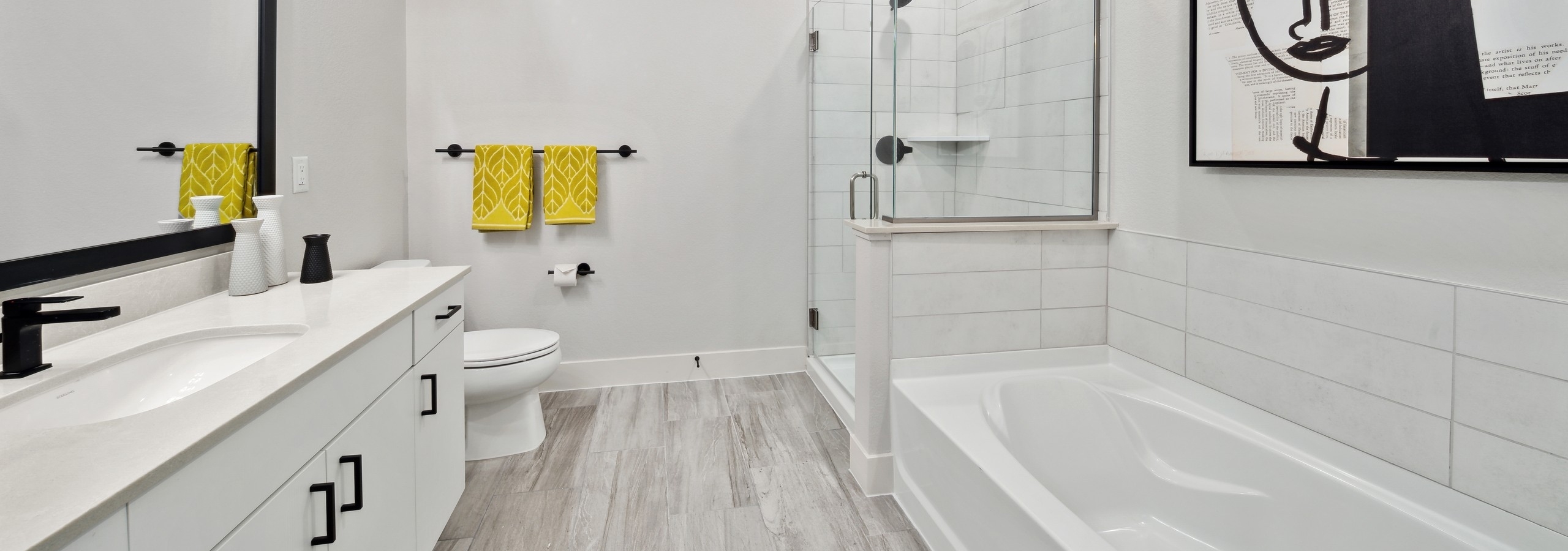 Bathroom at AMLI RiNo with large white tile shower and tub surrounds and white vanity with black hardware and gray wood floors