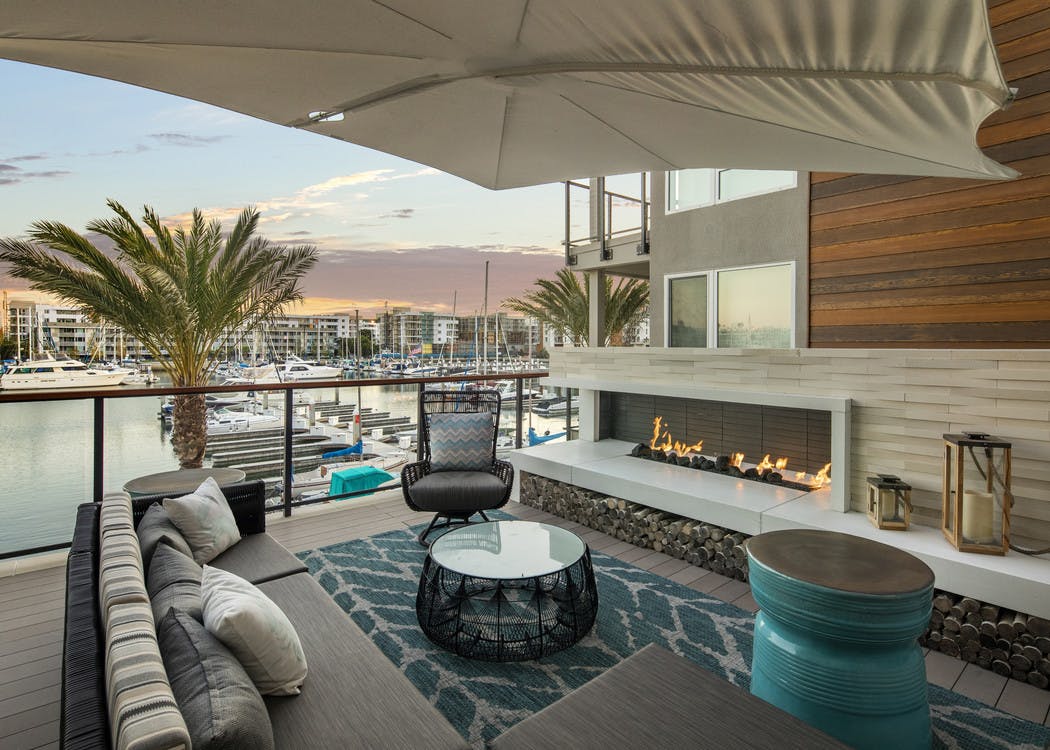Daytime view of AMLI Marina Del Rey apartment outdoor lounge with cozy seating, area rug and fireplace overlooking the marina