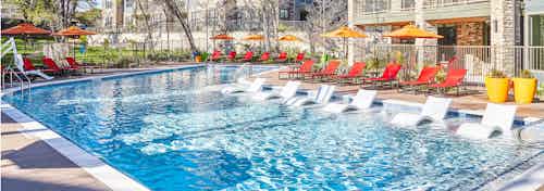 Daytime view of AMLI Covered Bridge resort-style pool with red lounge seating and light orange umbrellas for shade