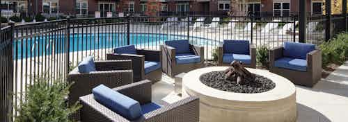 Exterior of courtyard at AMLI Deerfield with closeup of firepit and a swimming pool in background with lounge chairs