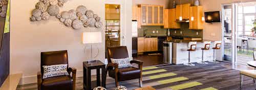 A clubroom at AMLI Arista apartments with a kitchen and a counter top with bar stools and chairs with artwork on the walls