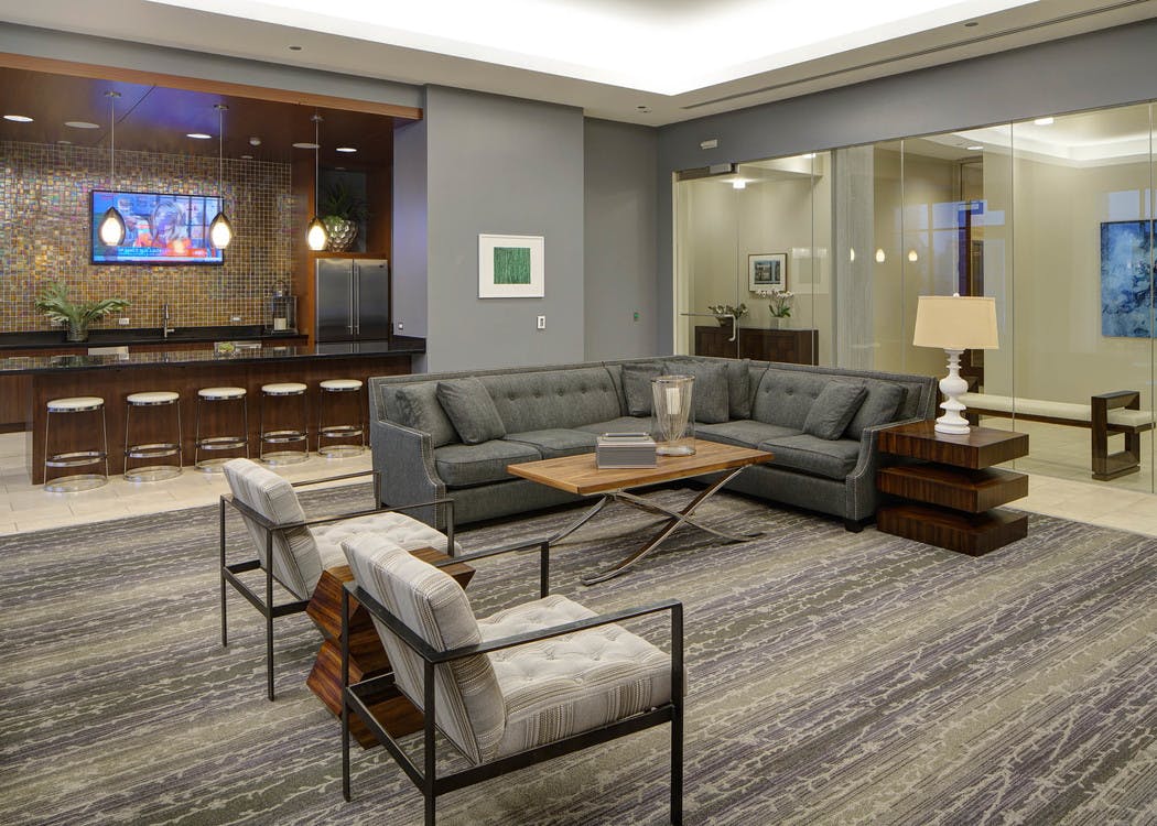 AMLI River North lounge with luxurious gray and neutral toned furniture in living room set up and kitchen in background with five sitting stools at counter.