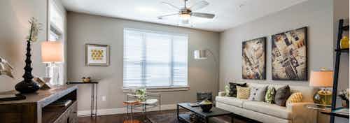 Interior view of a living room at AMLI Arista apartments with a couch and coffee table and a ceiling fan as well as windows