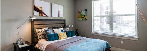 Interior view of a bedroom at AMLI Arista apartments with bed and crane lamp and large window with view of adjacent building