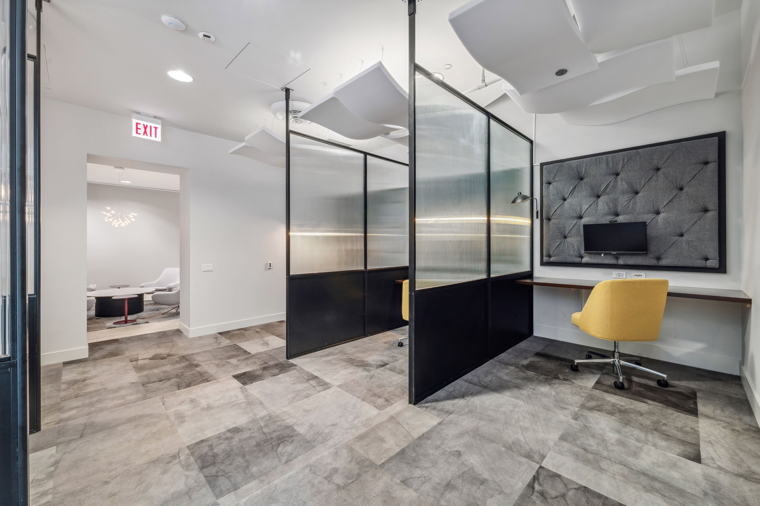 AMLI River North co working space with private desks separated by glass dividers with yellow chairs and mounted monitors 