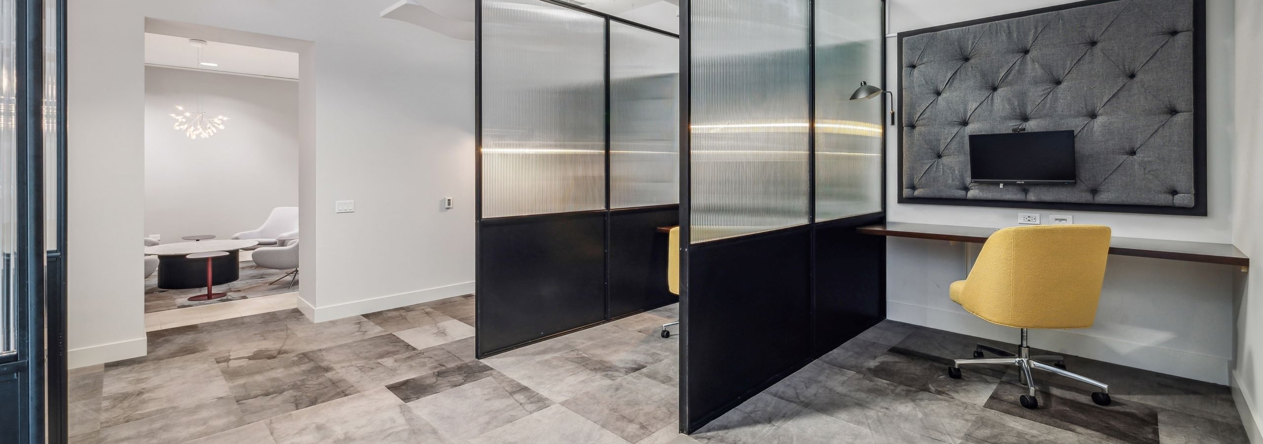 AMLI River North co working space with private desks separated by glass dividers with yellow chairs and mounted monitors