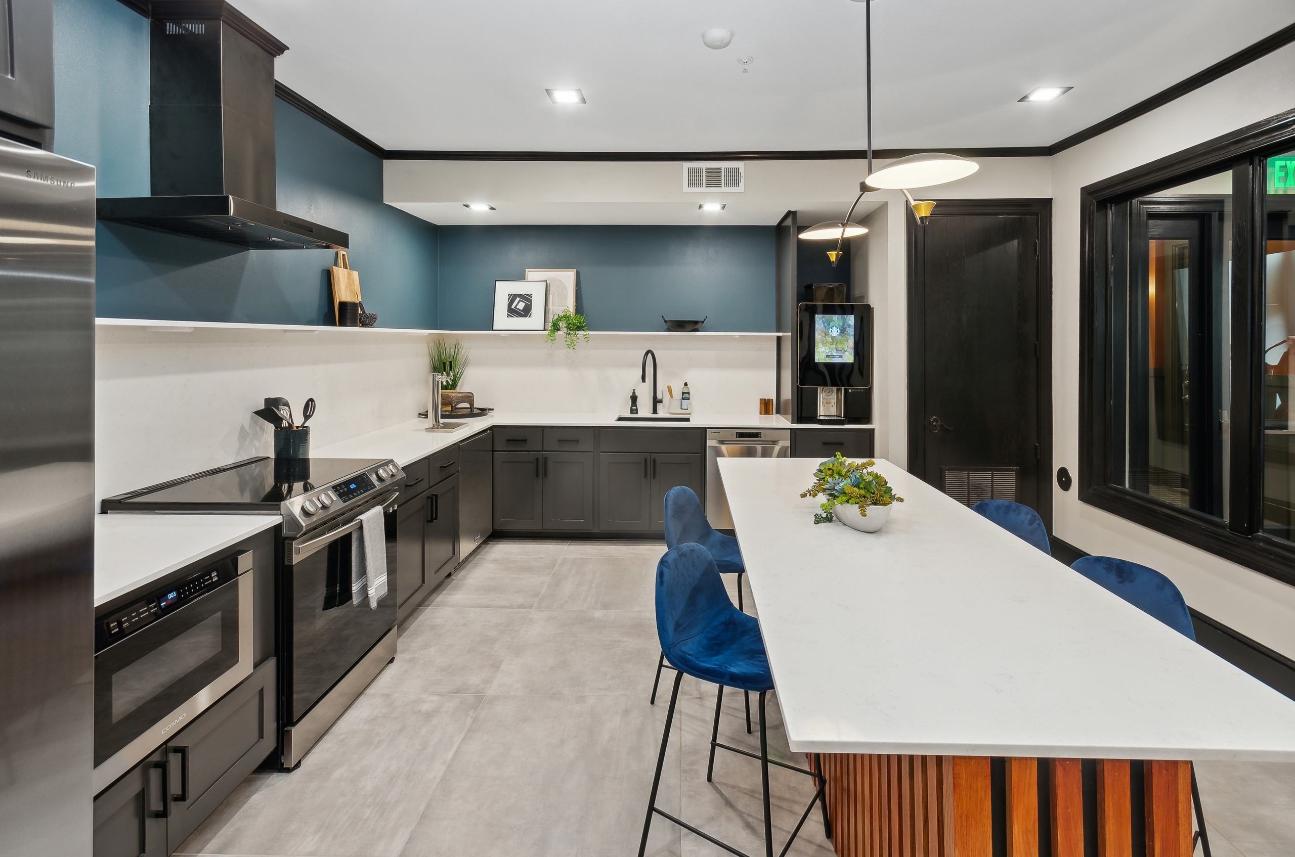 AMLI Campion Trail resident kitchen with stainless steel appliance and long white island with blue chairs and coffee station