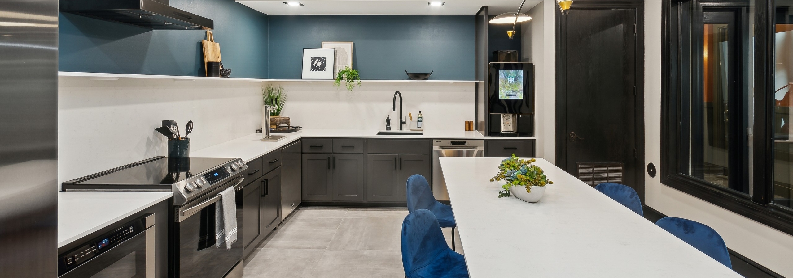 AMLI Campion Trail resident kitchen with stainless steel appliance and long white island with blue chairs and coffee station