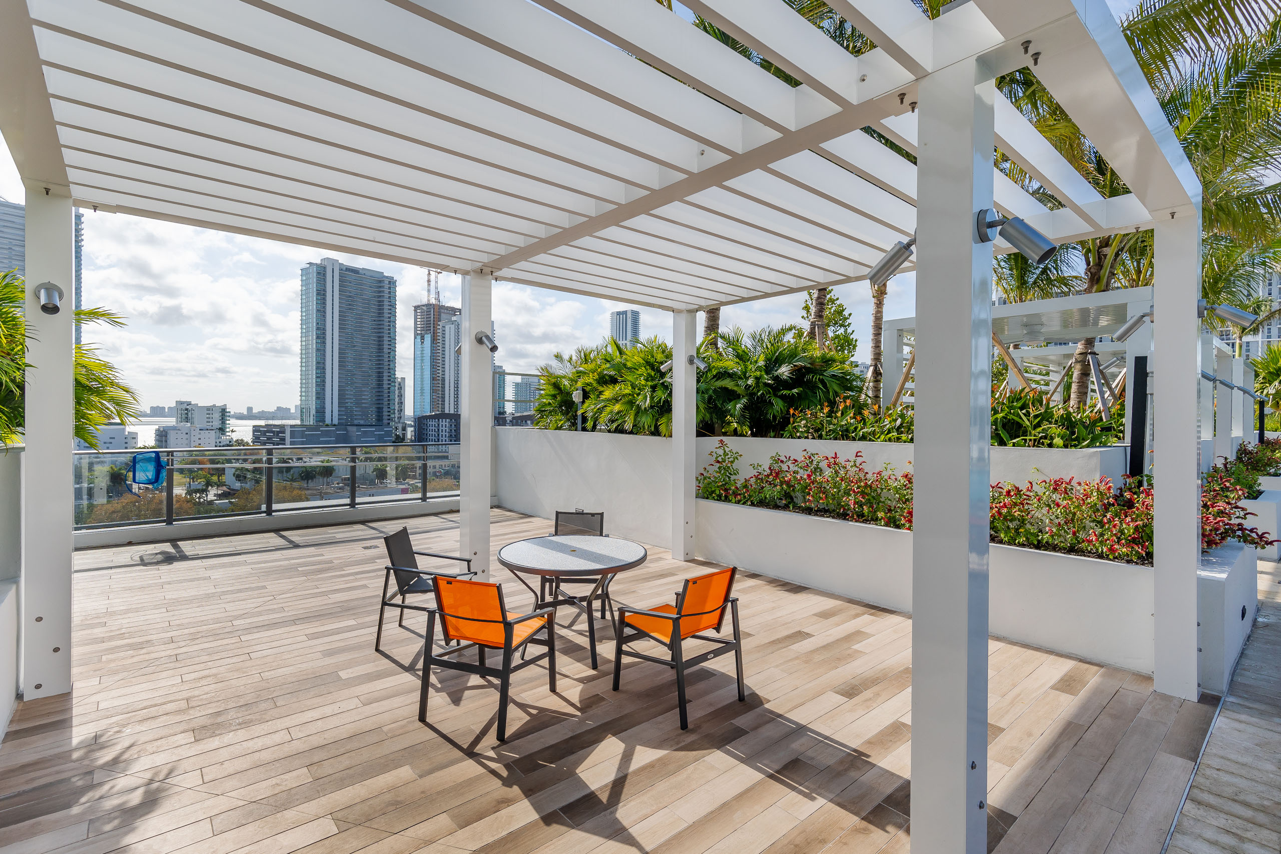 AMLI Midtown Miami rooftop deck with white pergola with table and chairs and wood tile floor with city view and lush landscape 