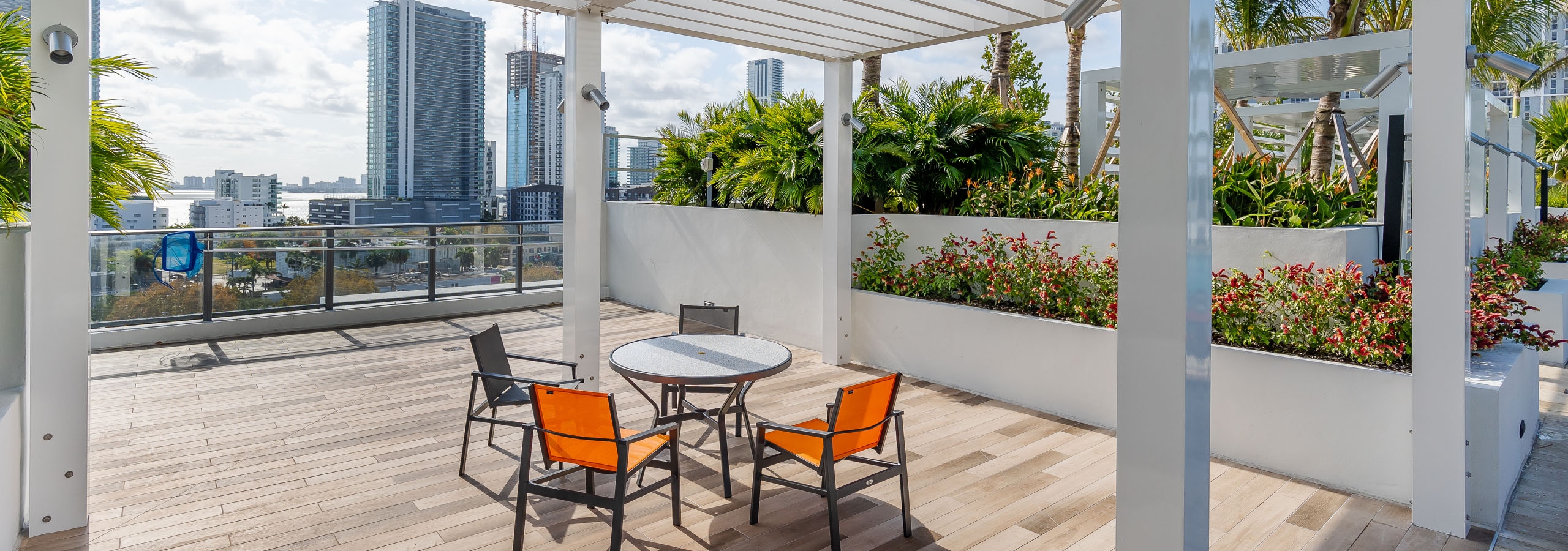 AMLI Midtown Miami rooftop deck with white pergola with table and chairs and wood tile floor with city view and lush landscape