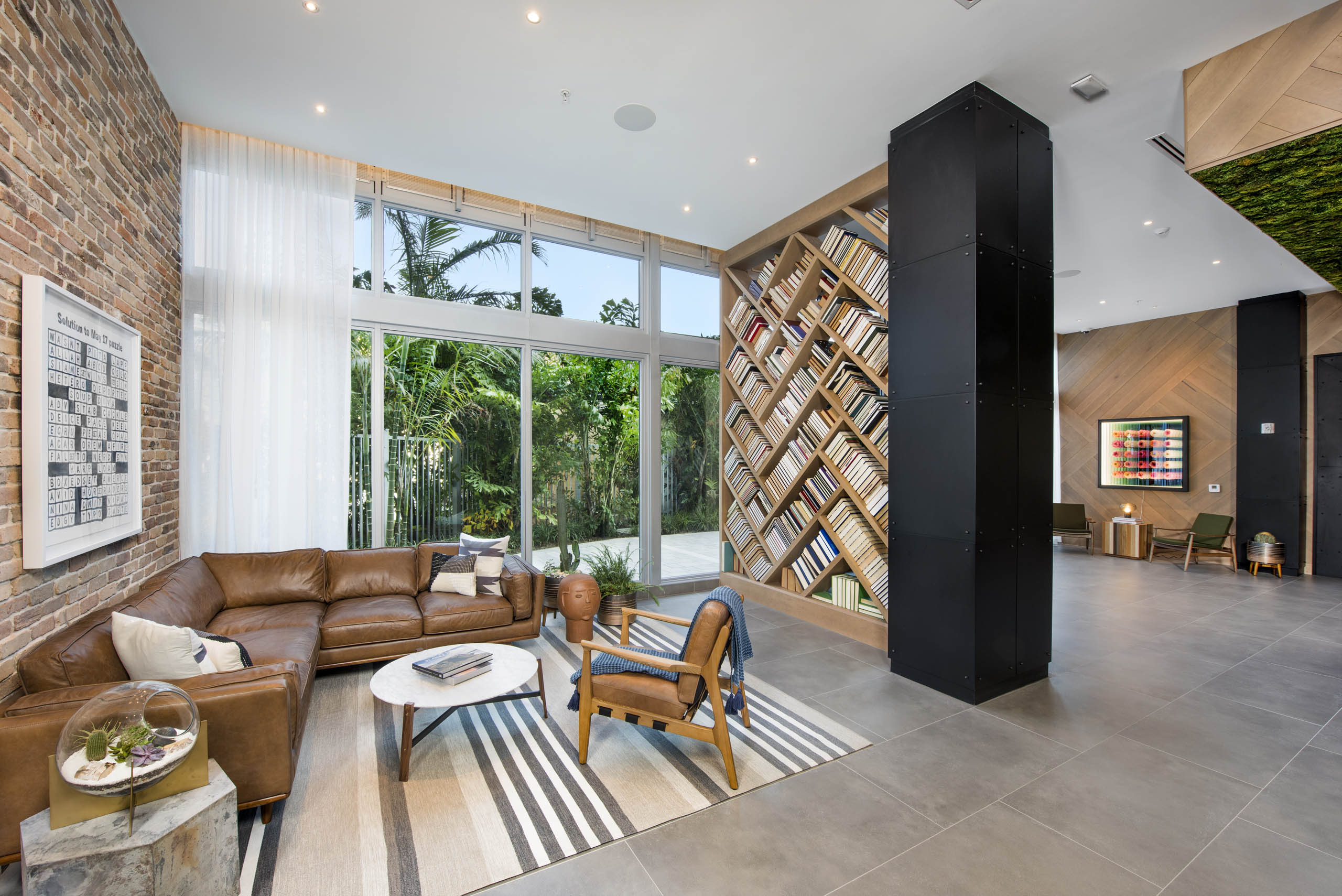 Clubhouse at AMLI Midtown 29 with book accent wall and leather couch with outside greenery view and brick and wood walls