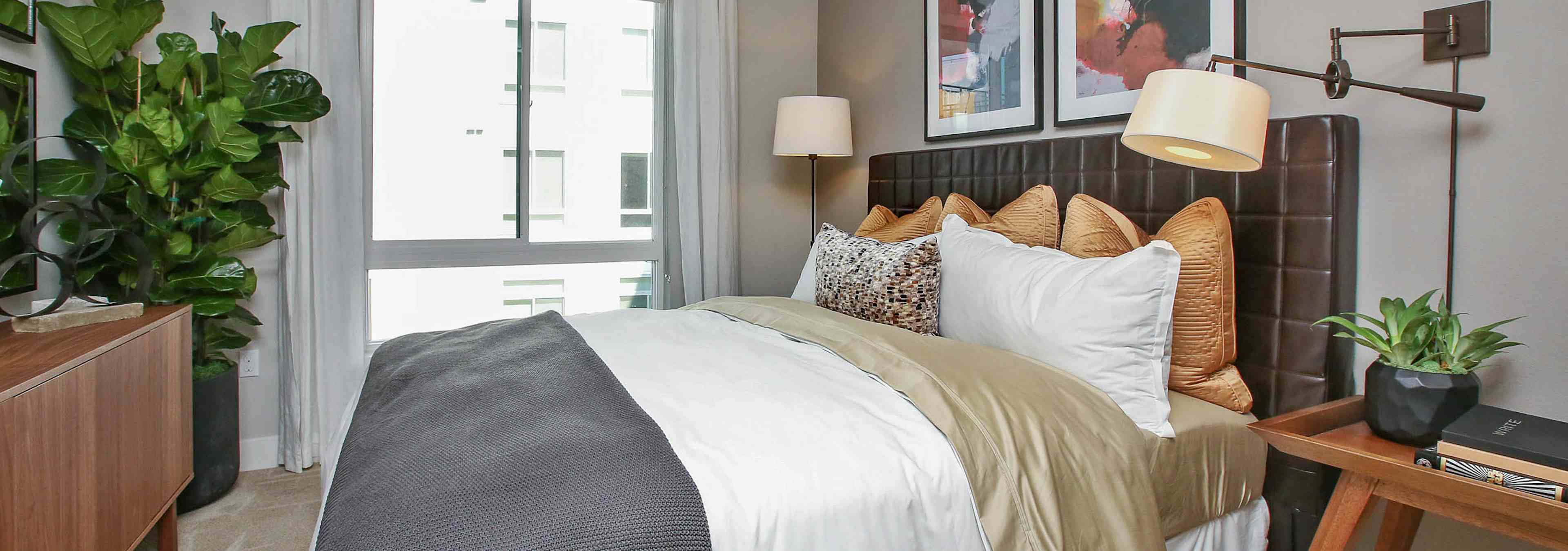 Interior of AMLI Uptown Orange apartment bedroom with king bed with grey walls and night stand in front of large window