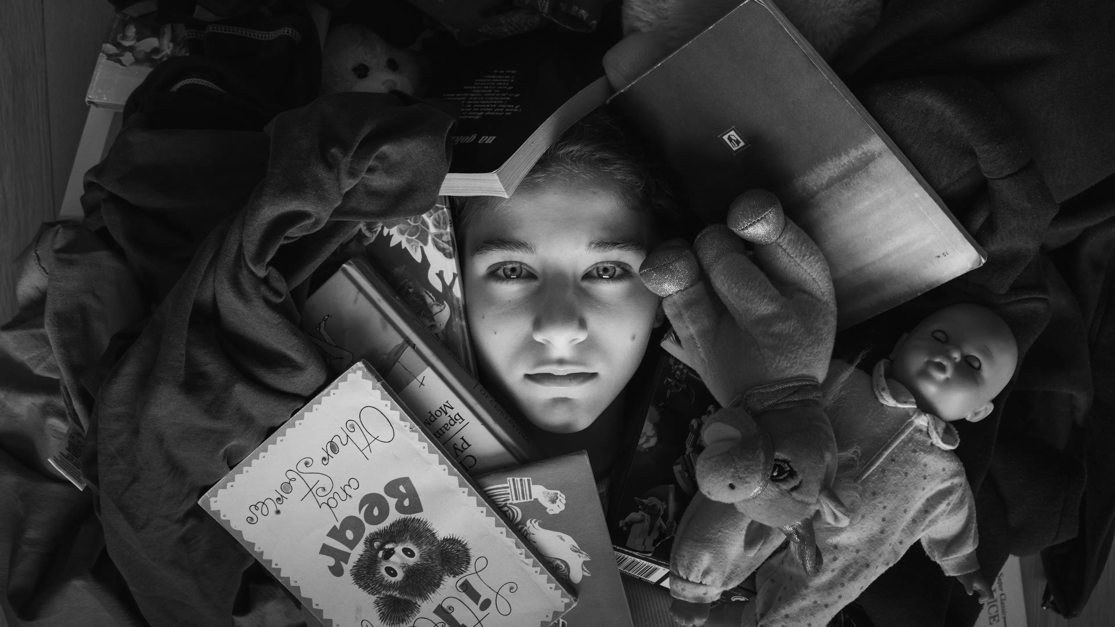 A young boy lying on the floor completely surrounded by toys and clutter
