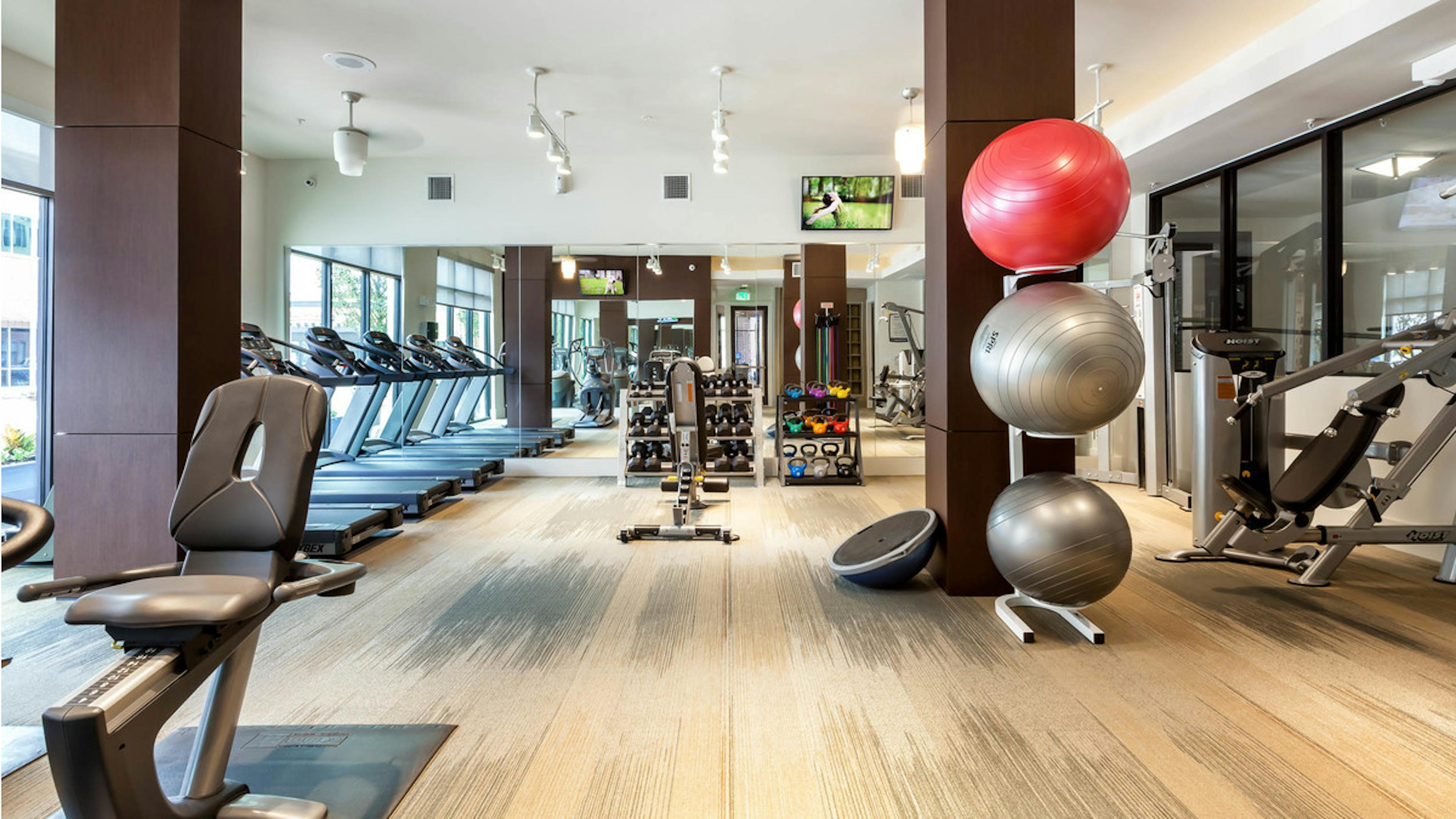 Fitness center at AMLI West Plano with floor to ceiling windows and a variety of cardio and weight exercise equipment