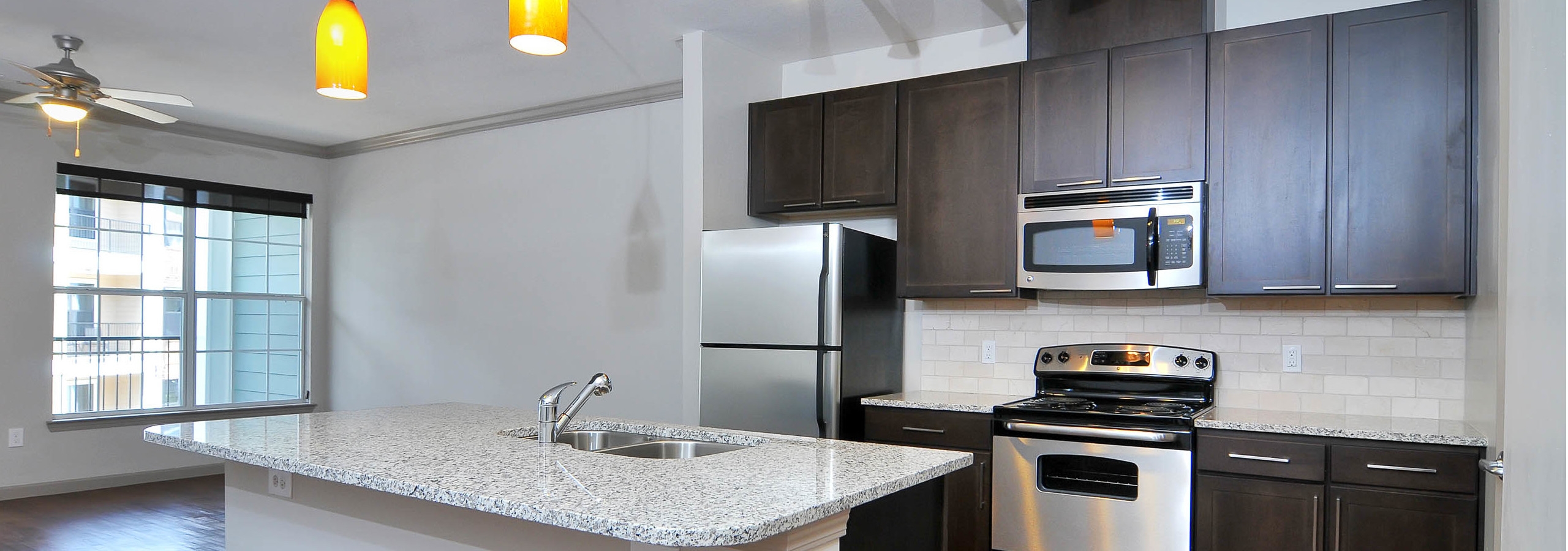 AMLI North Point kitchen with a wide island and modern hanging light fixtures connecting to living area with a large window