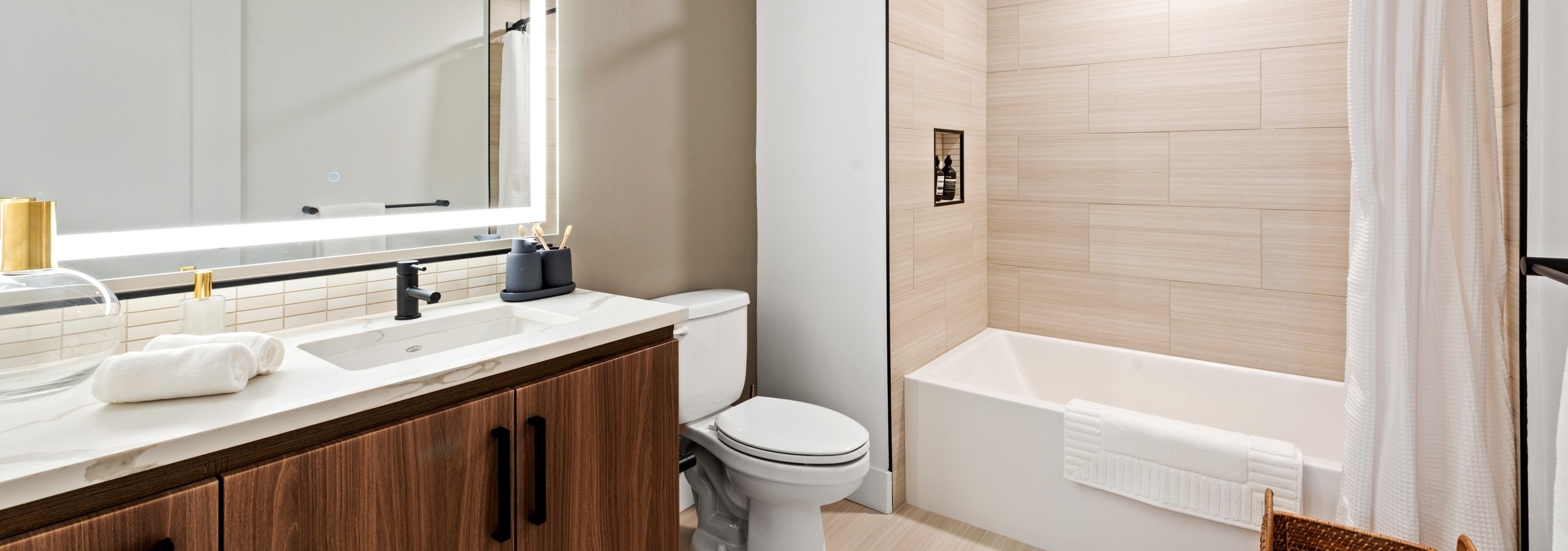 Interior view of AMLI Old Pasadena apartment bathroom with dark cabinetry and quartz countertop and lighted framed mirror