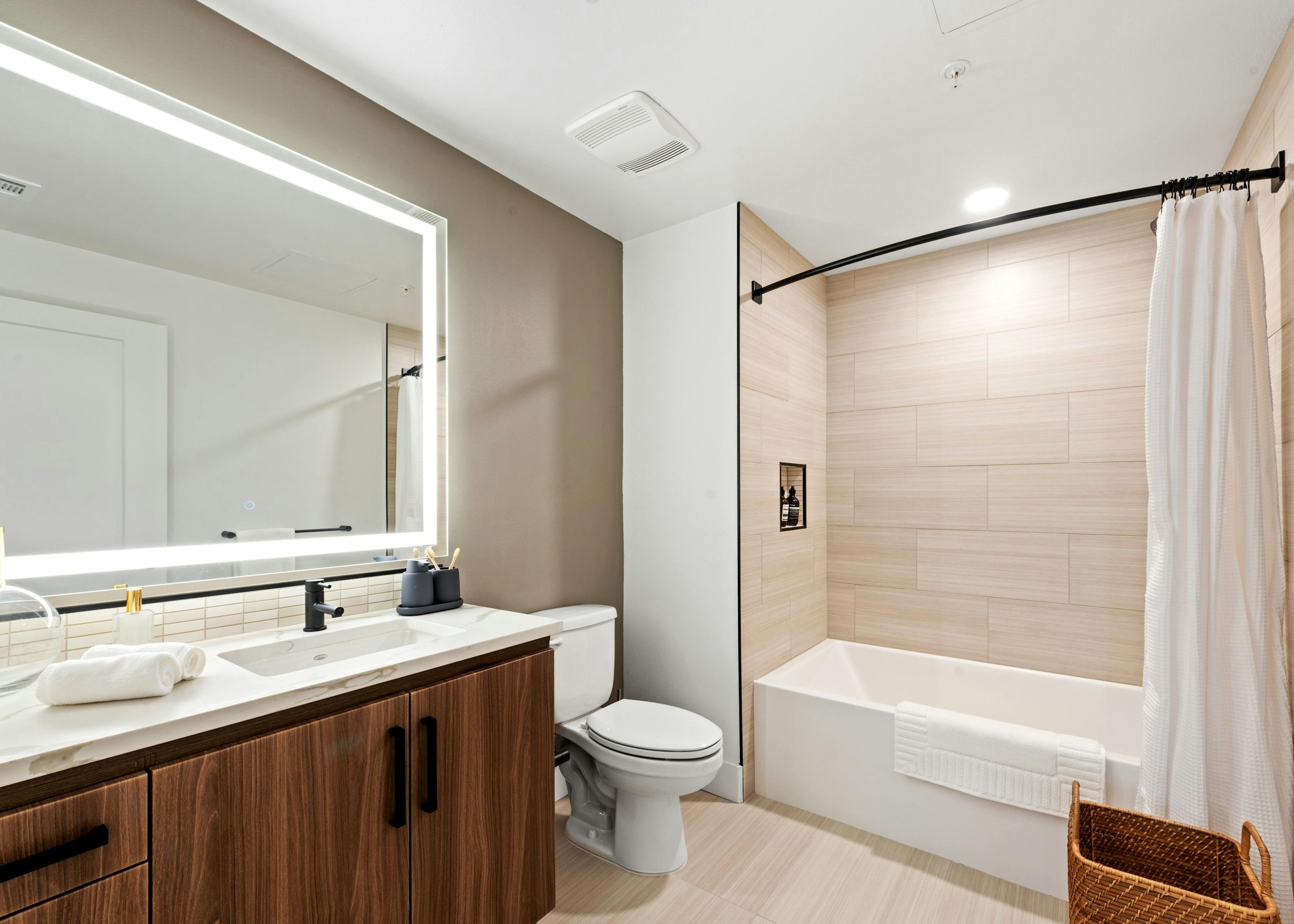 Interior view of AMLI Old Pasadena apartment bathroom with dark cabinetry and quartz countertop and lighted framed mirror
