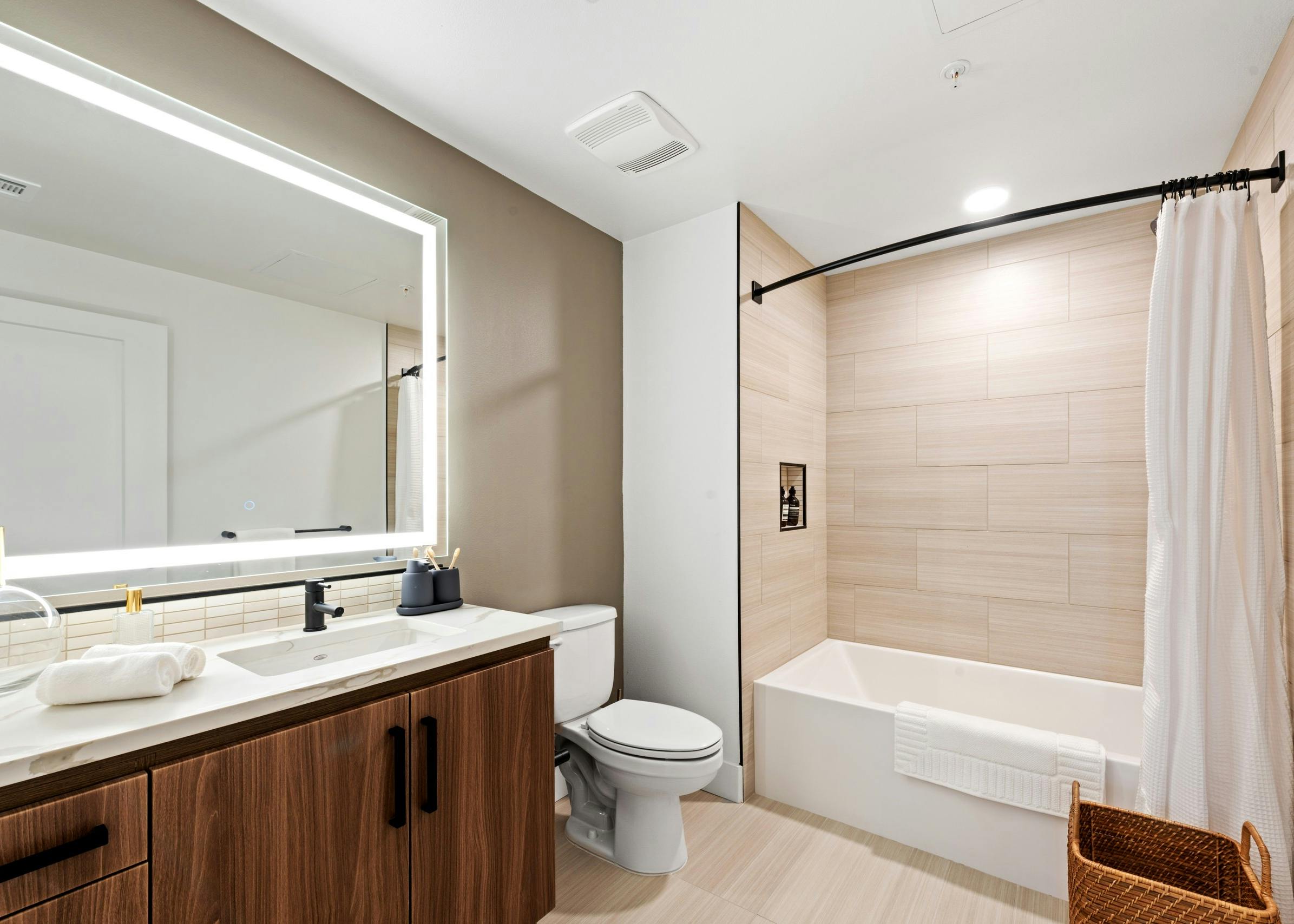 Interior view of AMLI Old Pasadena apartment bathroom with dark cabinetry and quartz countertop and lighted framed mirror