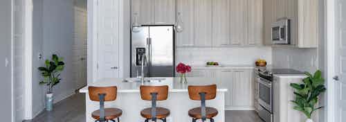 Kitchen at AMLI Arts Center with light wood cabinets and an island with three orange barstools and two faux floor plants
