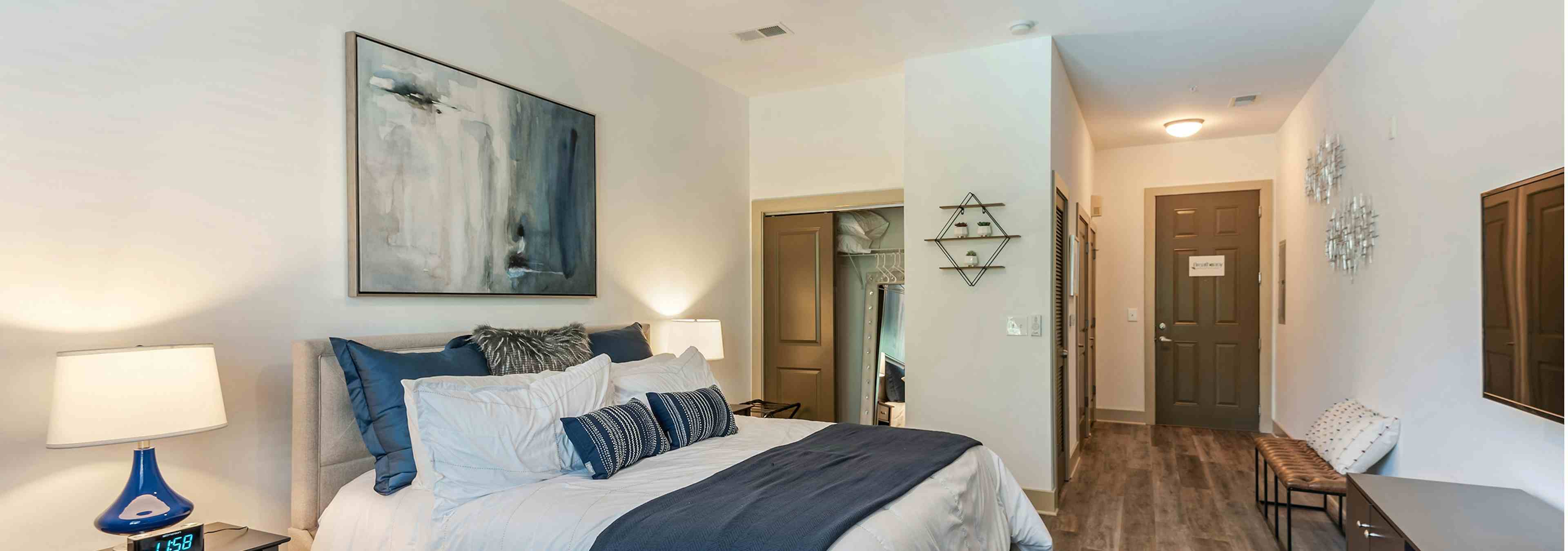 Interior view of AMLI Parkside bedroom with light hardwood and cream walls with blue decor and a peek into walk in closet