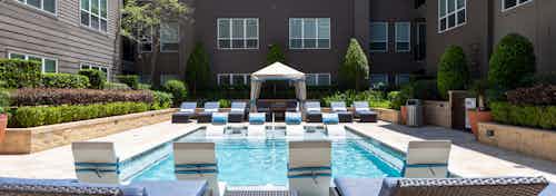 Daytime view of pool AMLI River Oaks apartment building showcasing cabana at far end and lounge seating at each end of pool