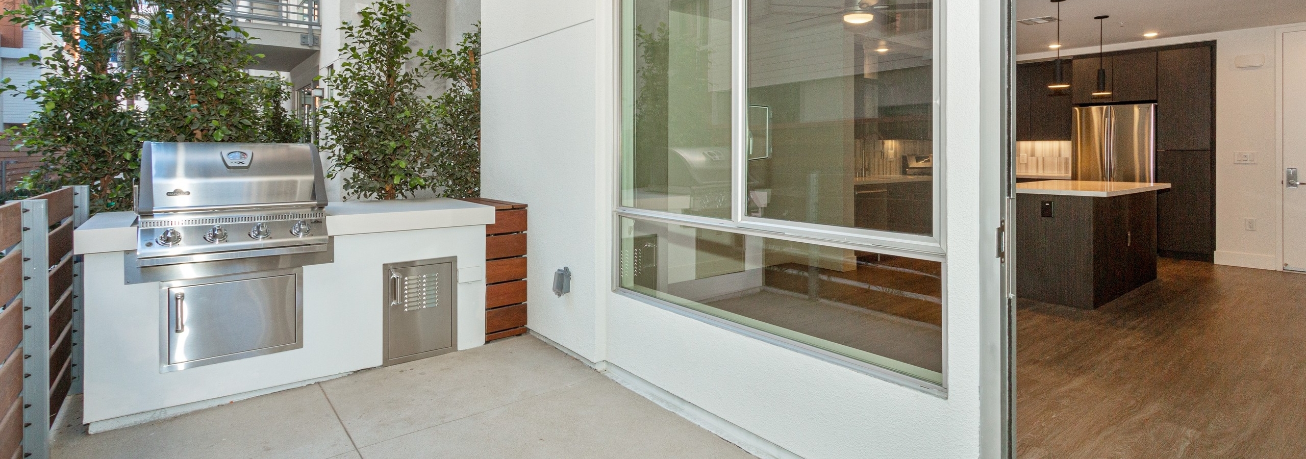 Daytime exterior view of private patio with BBQ grill facing into kitchen area at AMLI Park Broadway apartment building