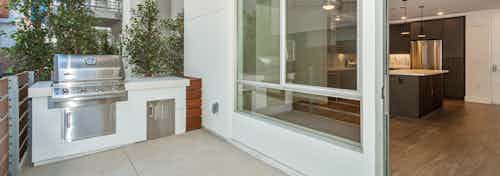 Daytime exterior view of private patio with BBQ grill facing into kitchen area at AMLI Park Broadway apartment building