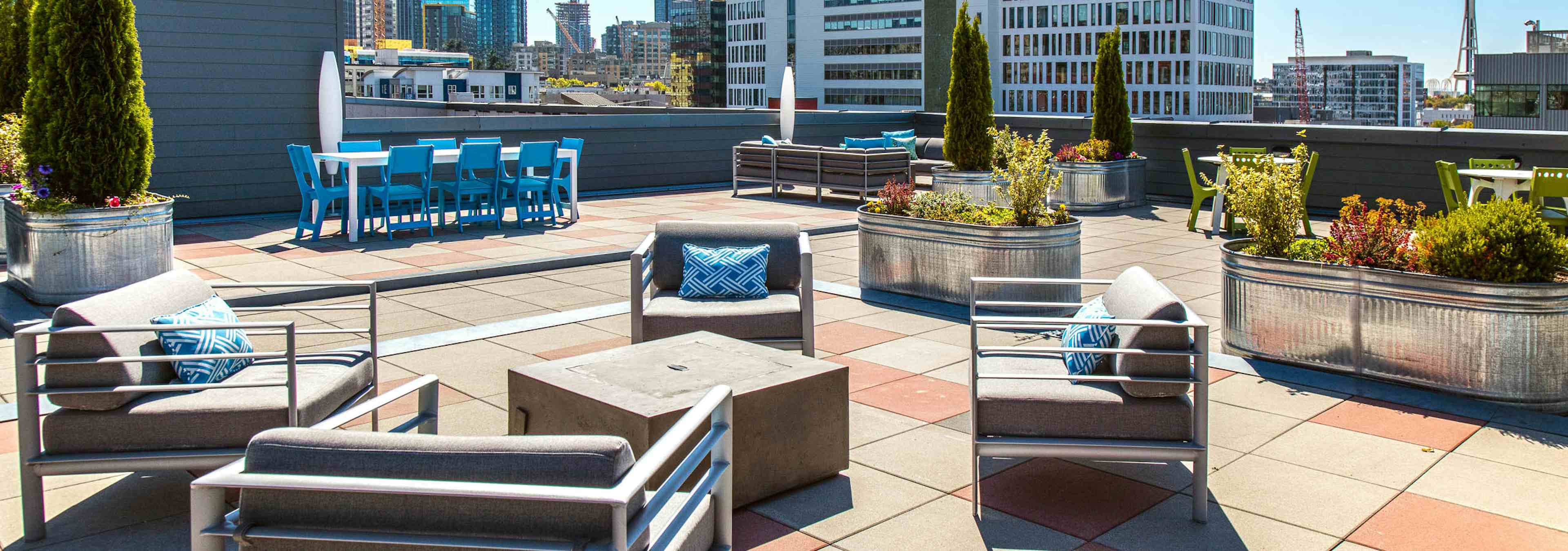 Daytime view of AMLI 535 apartment building rooftop deck with patio furniture fire pit bushes and view of Space Needle and downtown Seattle