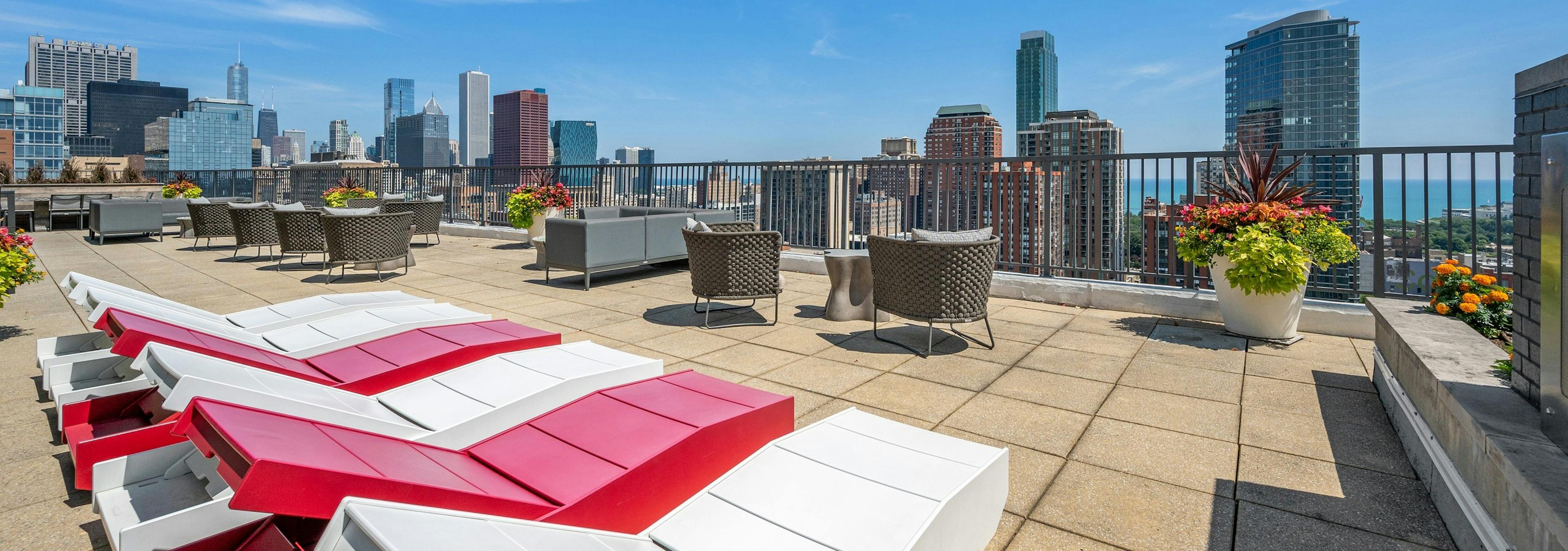 Rooftop with view of skyline at AMLI 900 with red and white wood lounge chairs and flower planters with chairs and tables