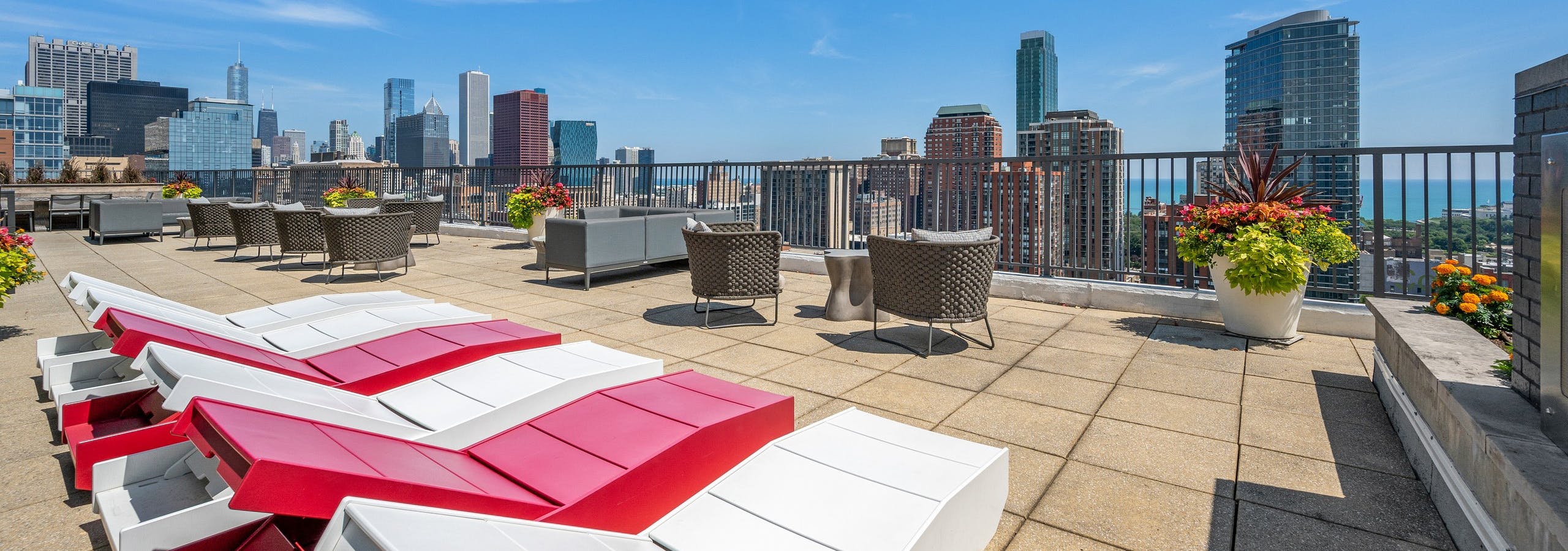 Rooftop with view of skyline at AMLI 900 with red and white wood lounge chairs and flower planters with chairs and tables