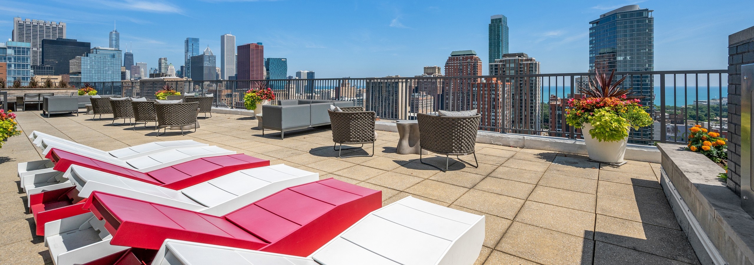 Rooftop with view of skyline at AMLI 900 with red and white wood lounge chairs and flower planters with chairs and tables