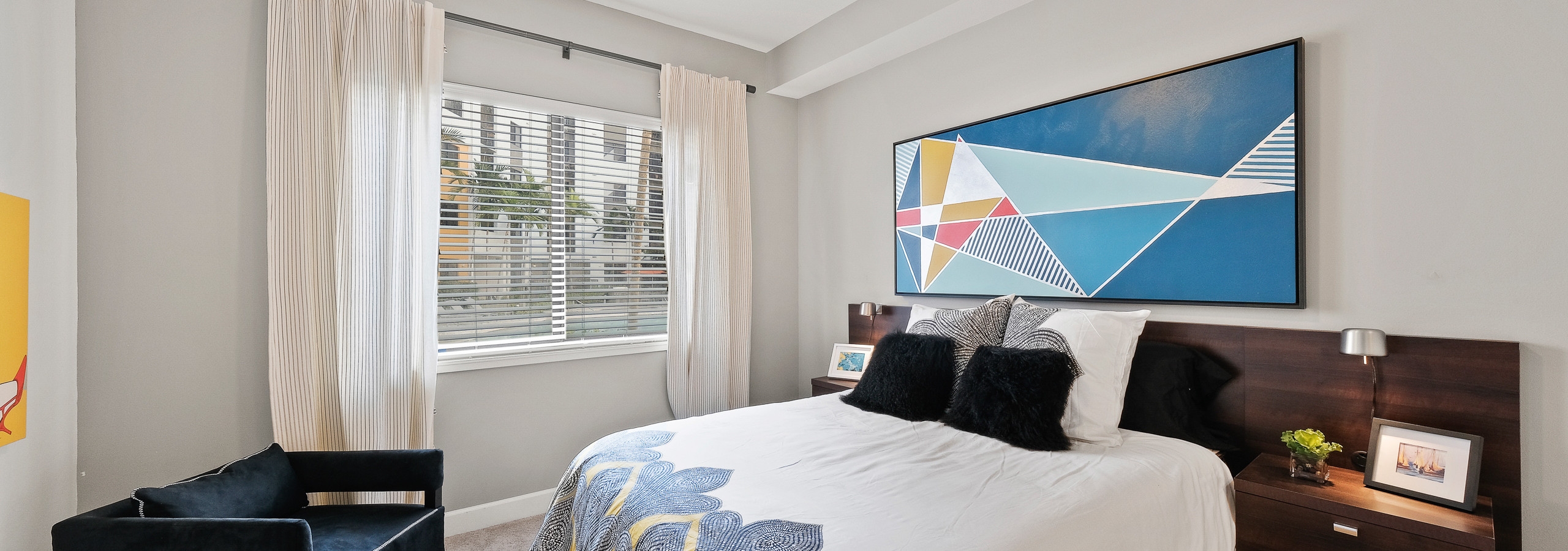 Interior view of an AMLI 8800 apartment bedroom with a bed underneath blue geometric wall art and a window view