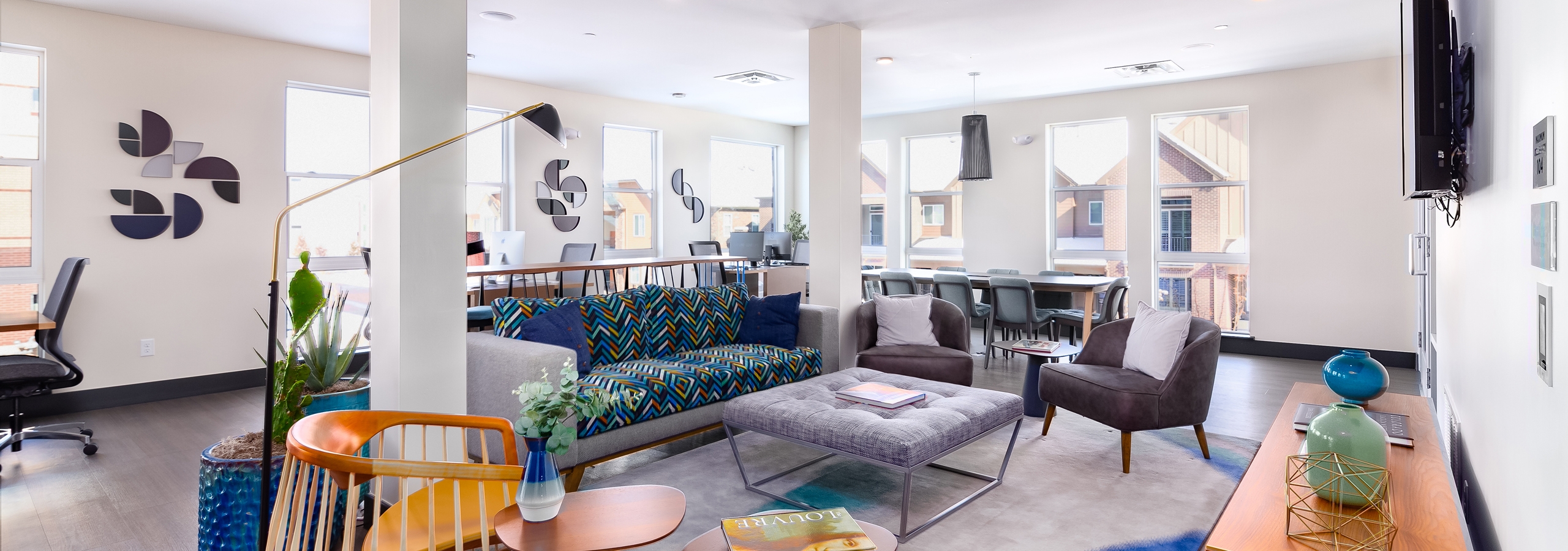 Interior of business center with computers, various multi-colored seating and mounted TV at AMLI Littleton Village apartments