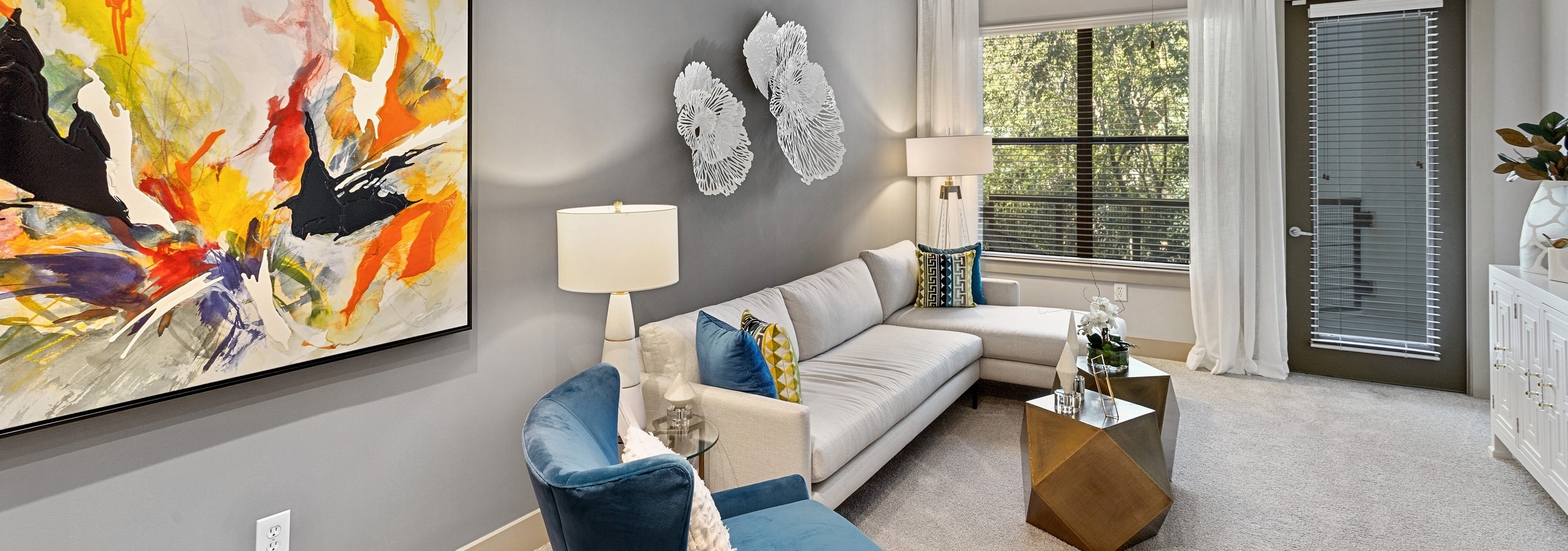 Interior of AMLI Parkside apartment living room with white sectional sofa and blue armchair in front of window and patio door