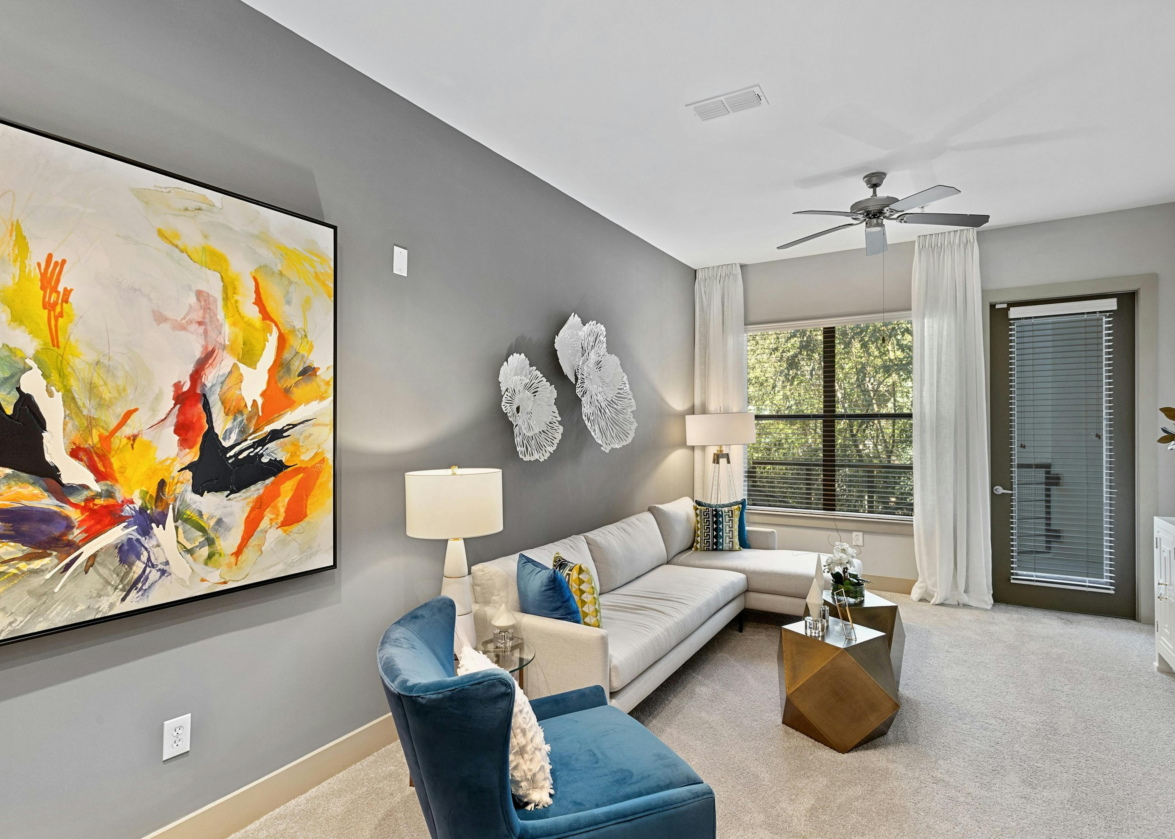Interior of AMLI Parkside apartment living room with white sectional sofa and blue armchair in front of window and patio door
