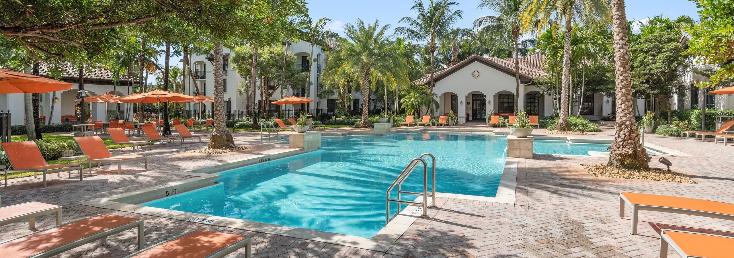 AMLI Toscana Place swimming pool with lush palm trees and orange lounge chairs and umbrellas with view of clubhouse
