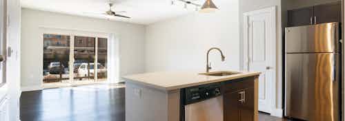Interior view of redesigned kitchen and living room at AMLI Inverness apartments with hard wood floor and glass sliding door