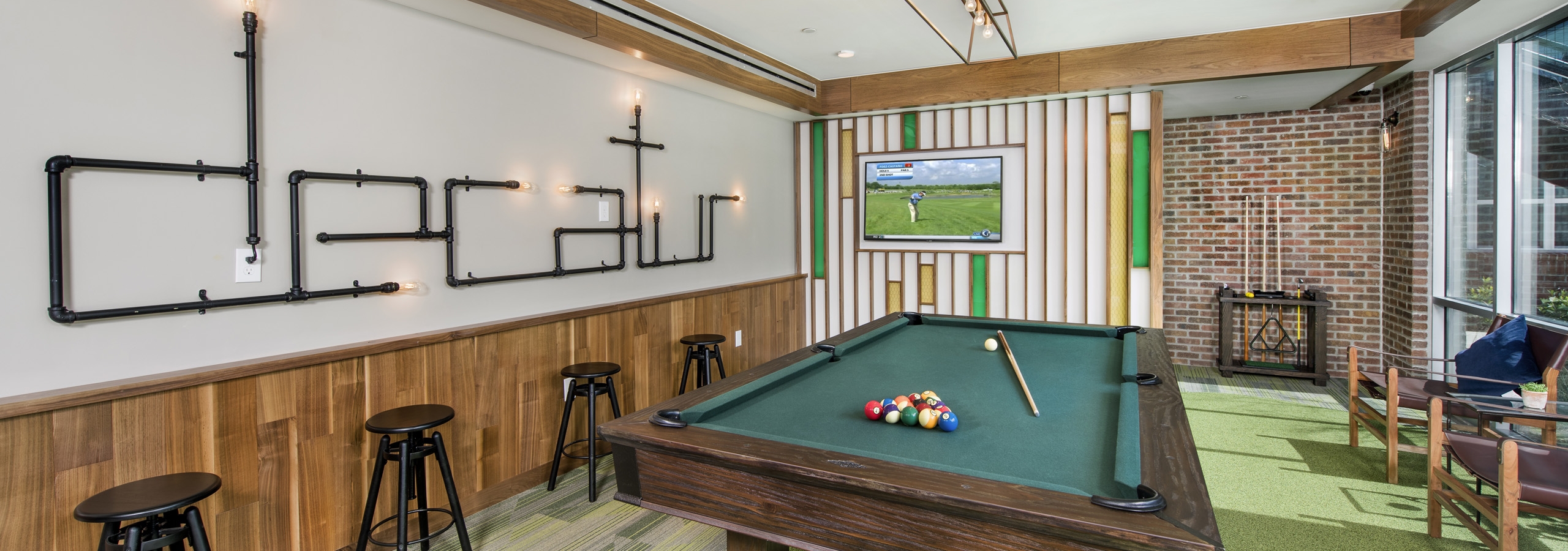 Clubroom at AMLI Decatur with billiards table set with balls and cue with a large screen TV and barstools on green carpet