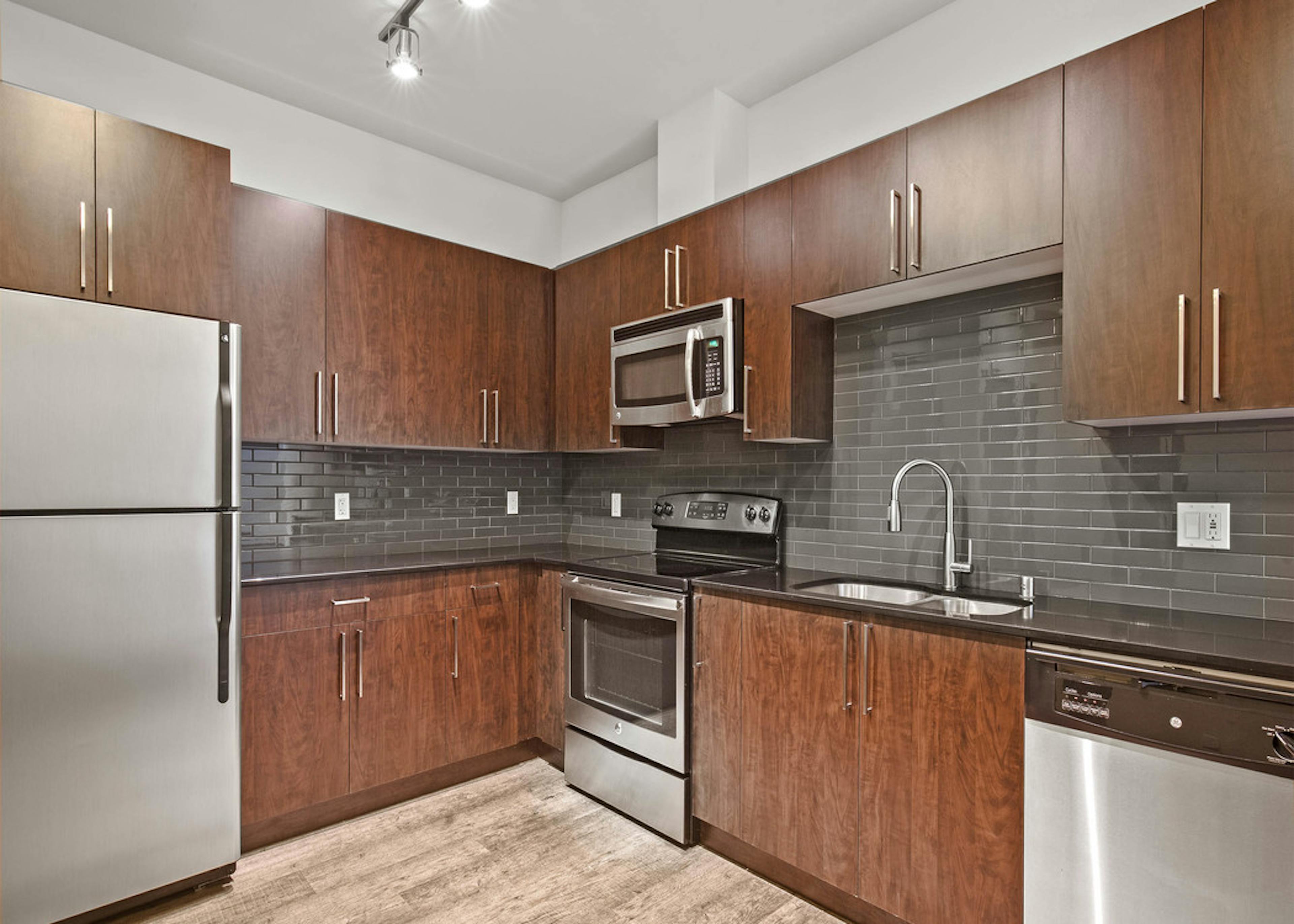 Interior view of AMLI Mark24 apartment kitchen with dark cabinets black back splash black quartz counter tops and stainless steel appliances 