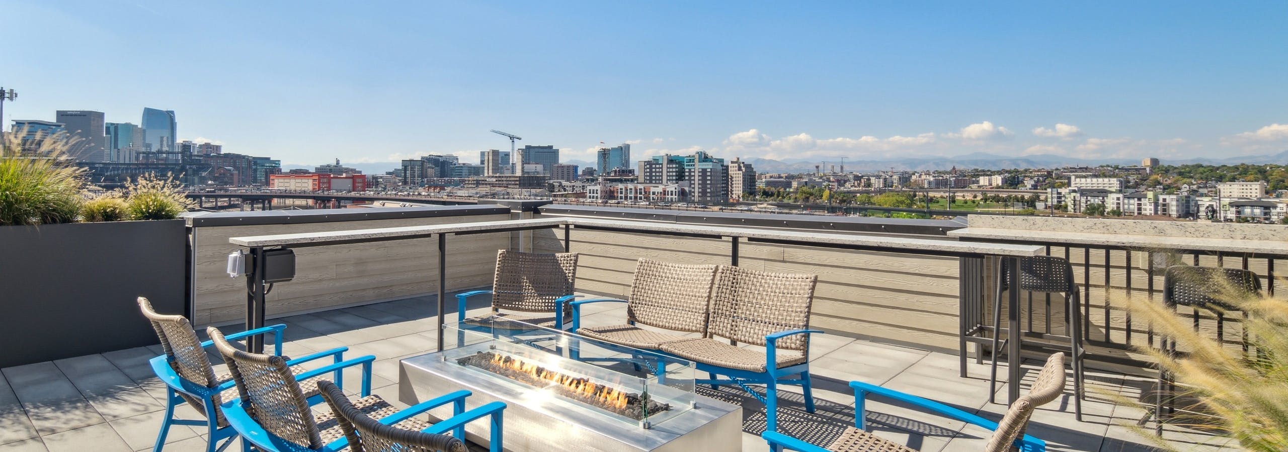 City view from the rooftop at AMLI RiNo apartments with blue and tan patio seating surrounding a lit rectangular fire pit