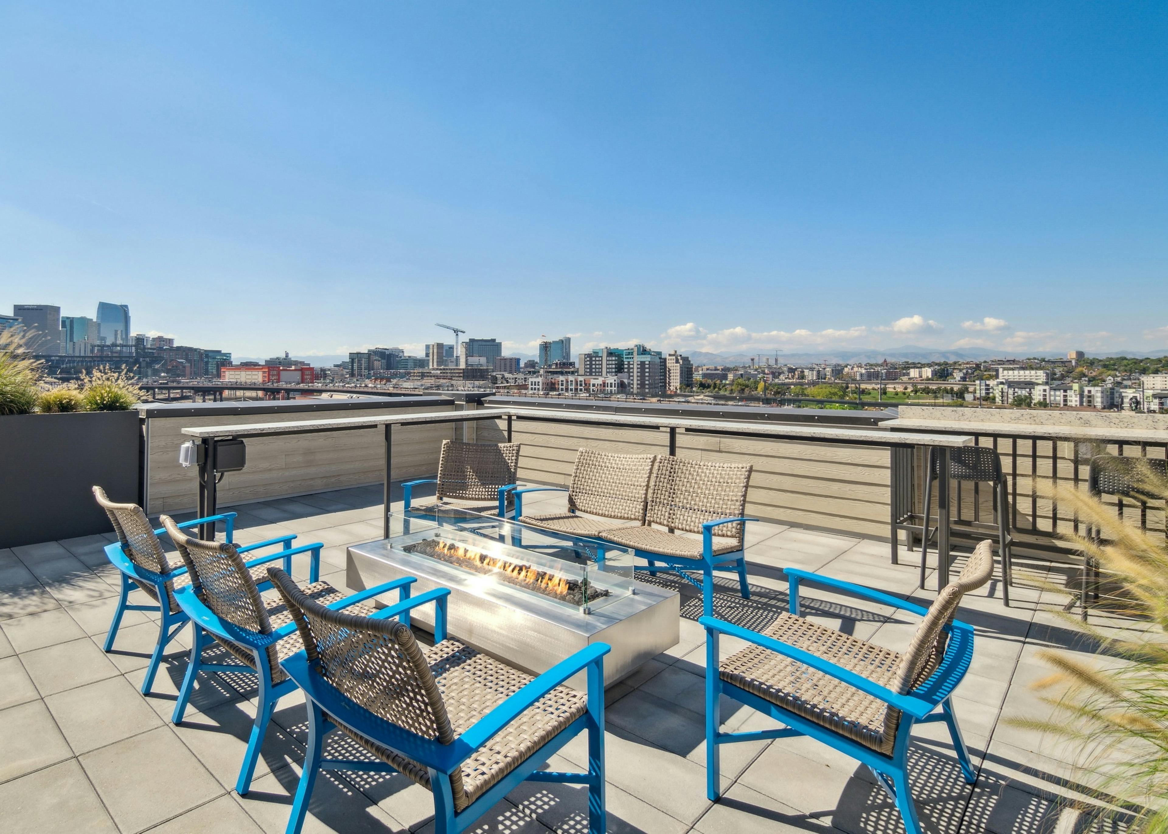 City view from the rooftop at AMLI RiNo apartments with blue and tan patio seating surrounding a lit rectangular fire pit