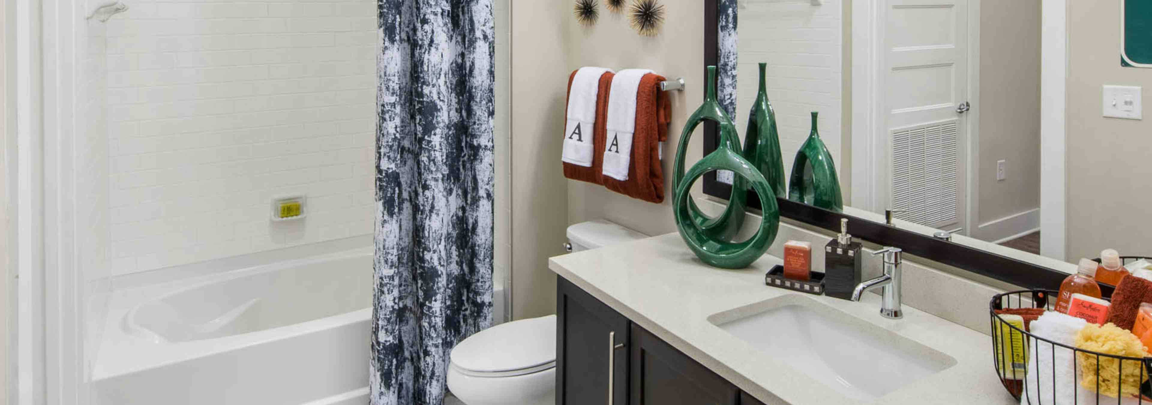 Bathroom at AMLI Buckhead with dark wood vanity sink and a white bathtub with a dark grey and white patterned curtain