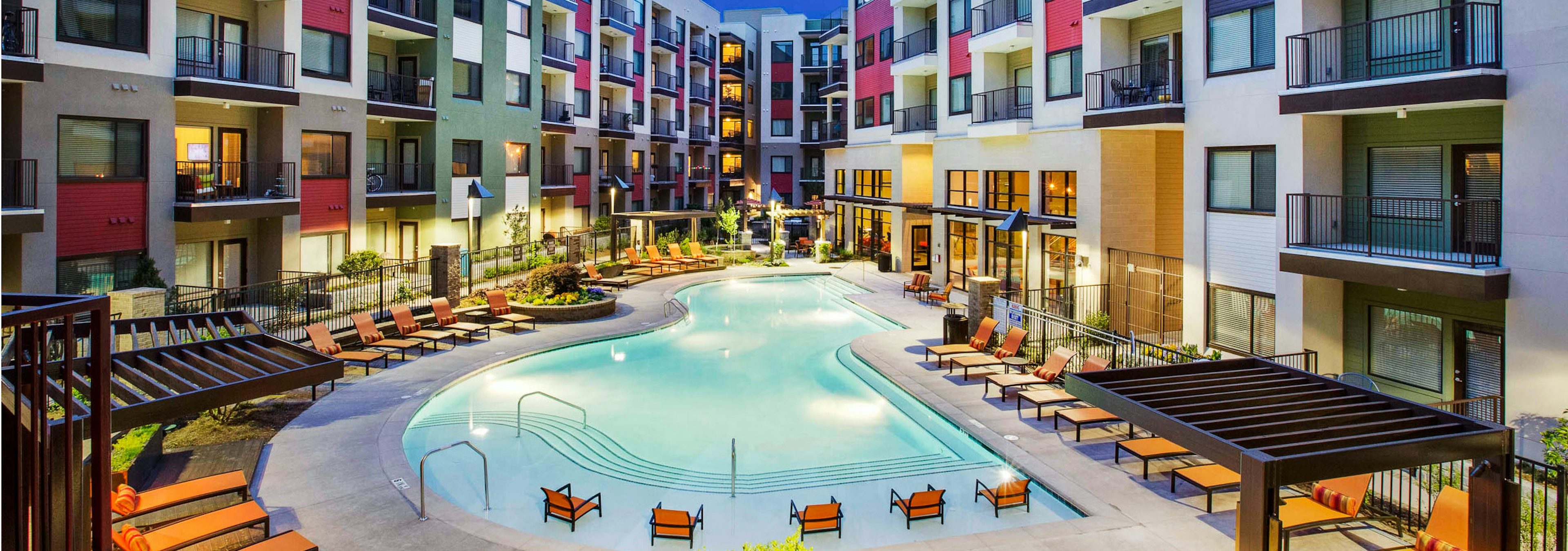 Nighttime view of the AMLI Ponce Park apartment swimming pool shaped like a teardrop and orange lounge seating with cabanas